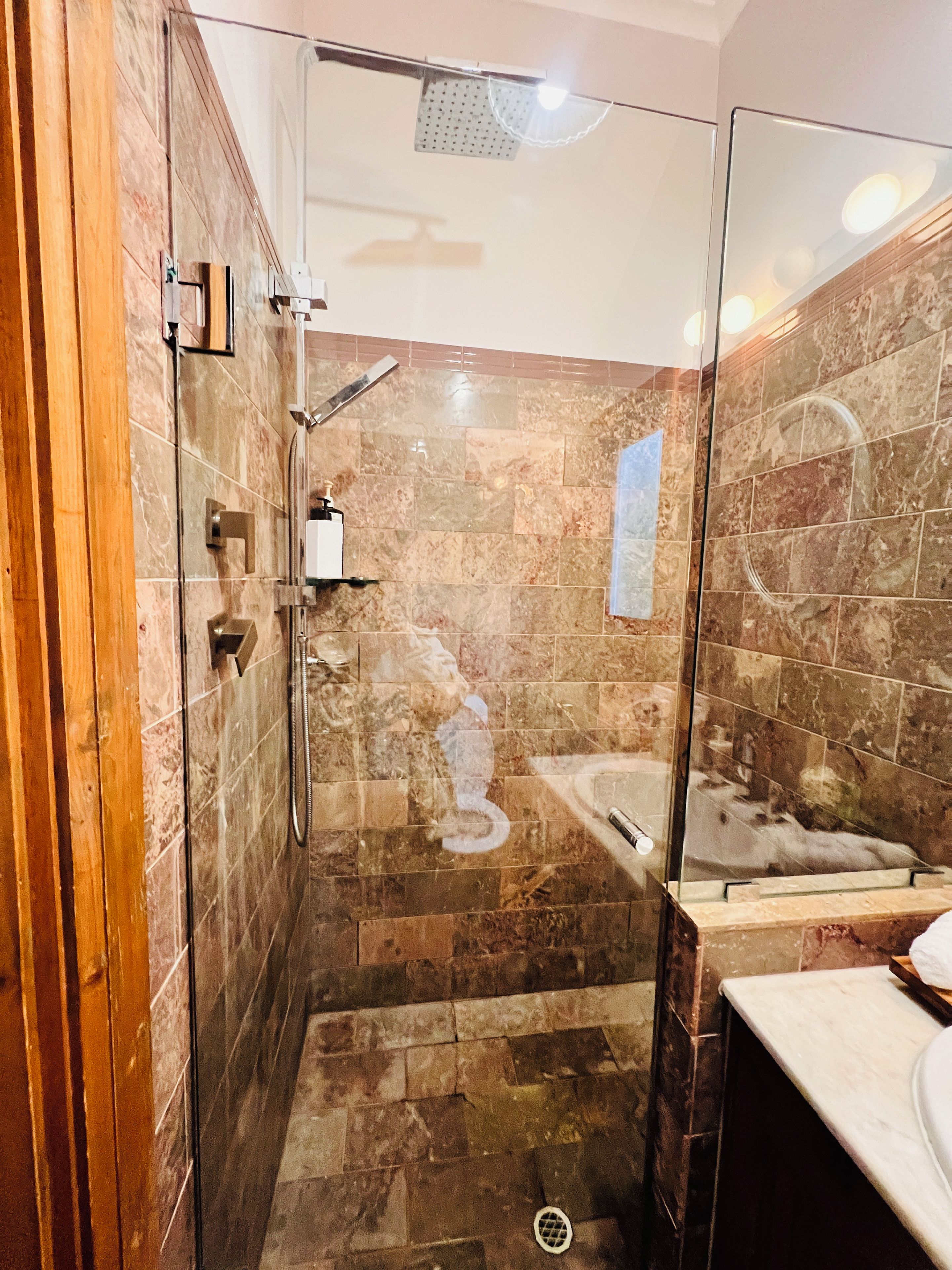 A modern bathroom with a glass-enclosed shower, a marble-tiled floor, and a visible bathtub.