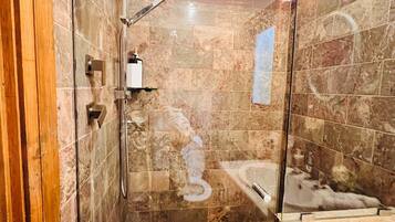 A modern bathroom with a glass-enclosed shower, a marble-tiled floor, and a visible bathtub.