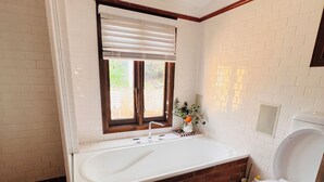 Une salle de bain avec une baignoire, des toilettes et une fenêtre avec des stores.