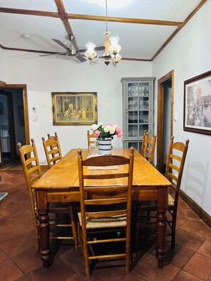 A dining room with a wooden table, six chairs, a chandelier, a ceiling fan, a painting, a cabinet with glass doors, and a framed picture on the wall.
