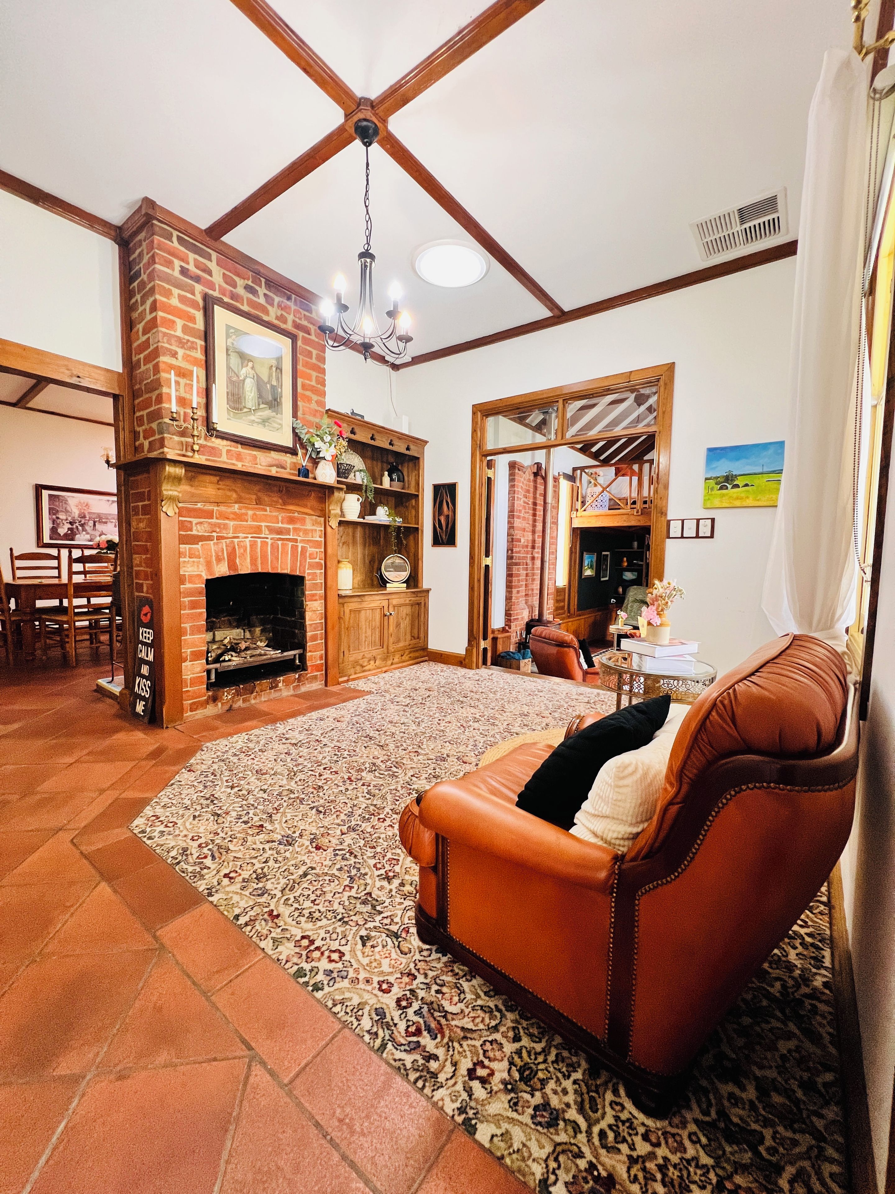 A living room with a fireplace, leather sofa, patterned rug, and a dining area with chairs.
