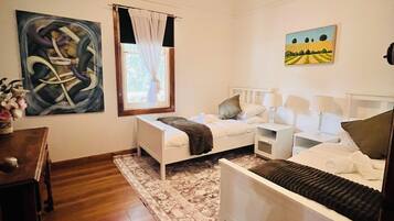 A bedroom with a bed, bedside tables, a ceiling fan, a window with curtains, and artwork on the walls.