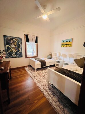 Ein Schlafzimmer mit einem Bett, Nachttischen, einem Deckenventilator, einem Fenster mit Vorhängen und Kunstwerken an den Wänden.