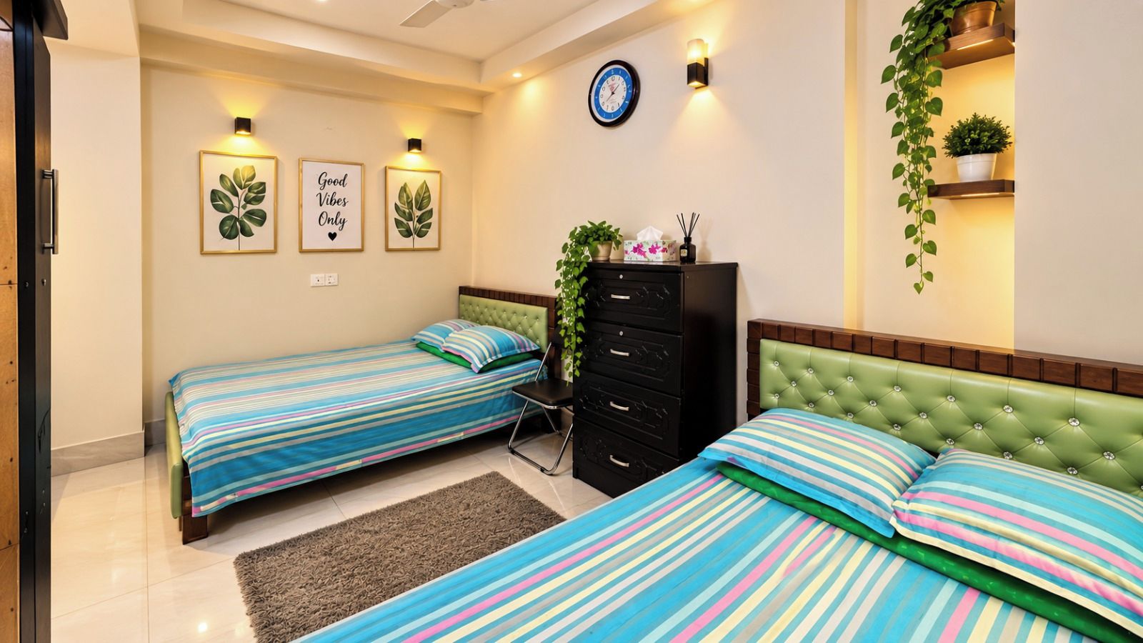 A bedroom with two single beds, a dresser, a clock, wall-mounted lights, and a potted plant.