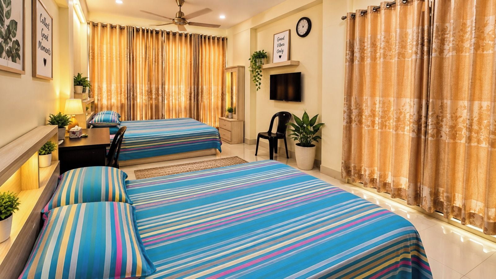 A hotel room with two beds, a desk, a chair, a TV, and a ceiling fan.