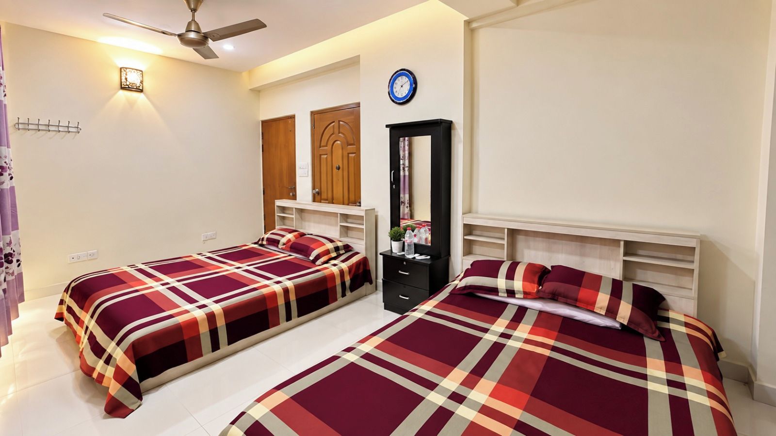 A hotel room with two beds, a wardrobe, a mirror, and a ceiling fan.