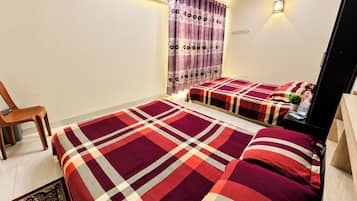 Un dormitorio con dos camas, una silla, una mesita de noche con una planta y una lámpara fijada a la pared.