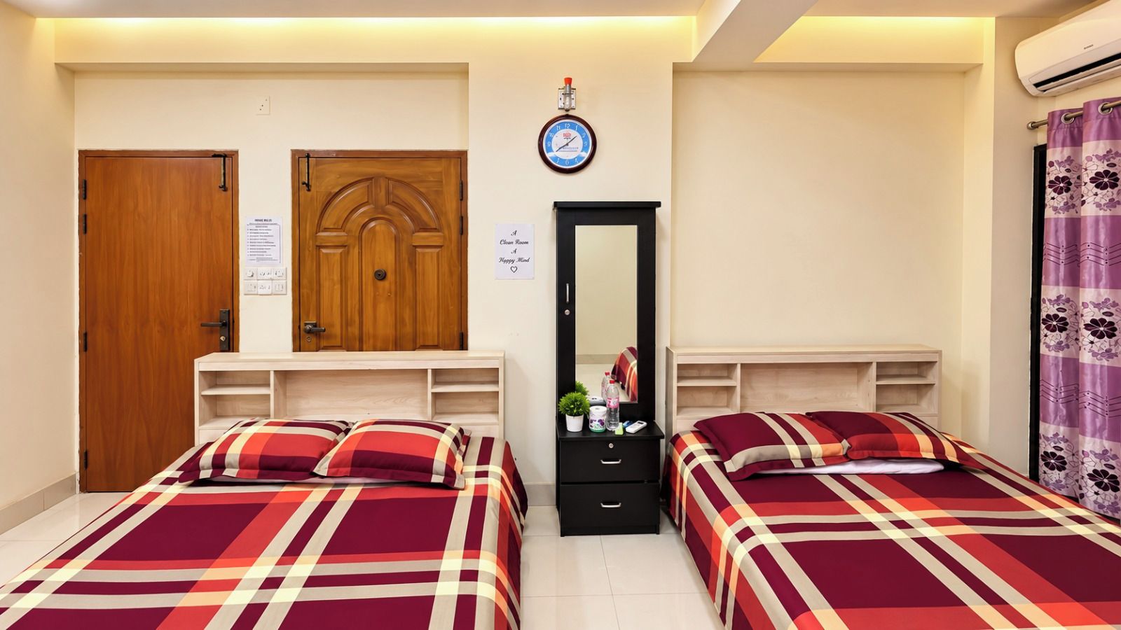 A bedroom with two beds, a wooden wardrobe, a mirror, and a clock on the wall.