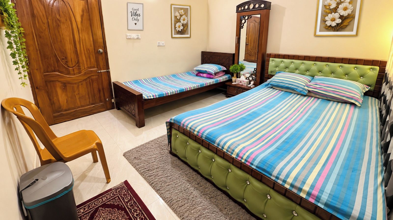 Une chambre avec un grand lit, deux petits lits, une armoire en bois, un miroir et une chaise.