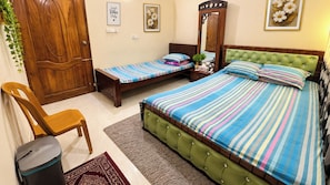 A bedroom with a large bed, two smaller beds, a wooden wardrobe, a mirror, and a chair.