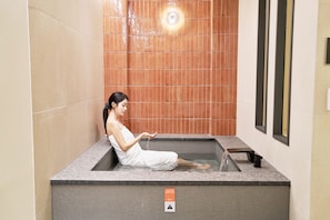 Una persona sentada en una bañera de hidromasaje con un letrero de precaución en el suelo.