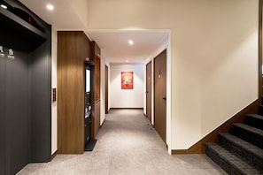 Un pasillo de hotel con piso alfombrado, un quiosco de autoservicio y una escalera a la derecha.