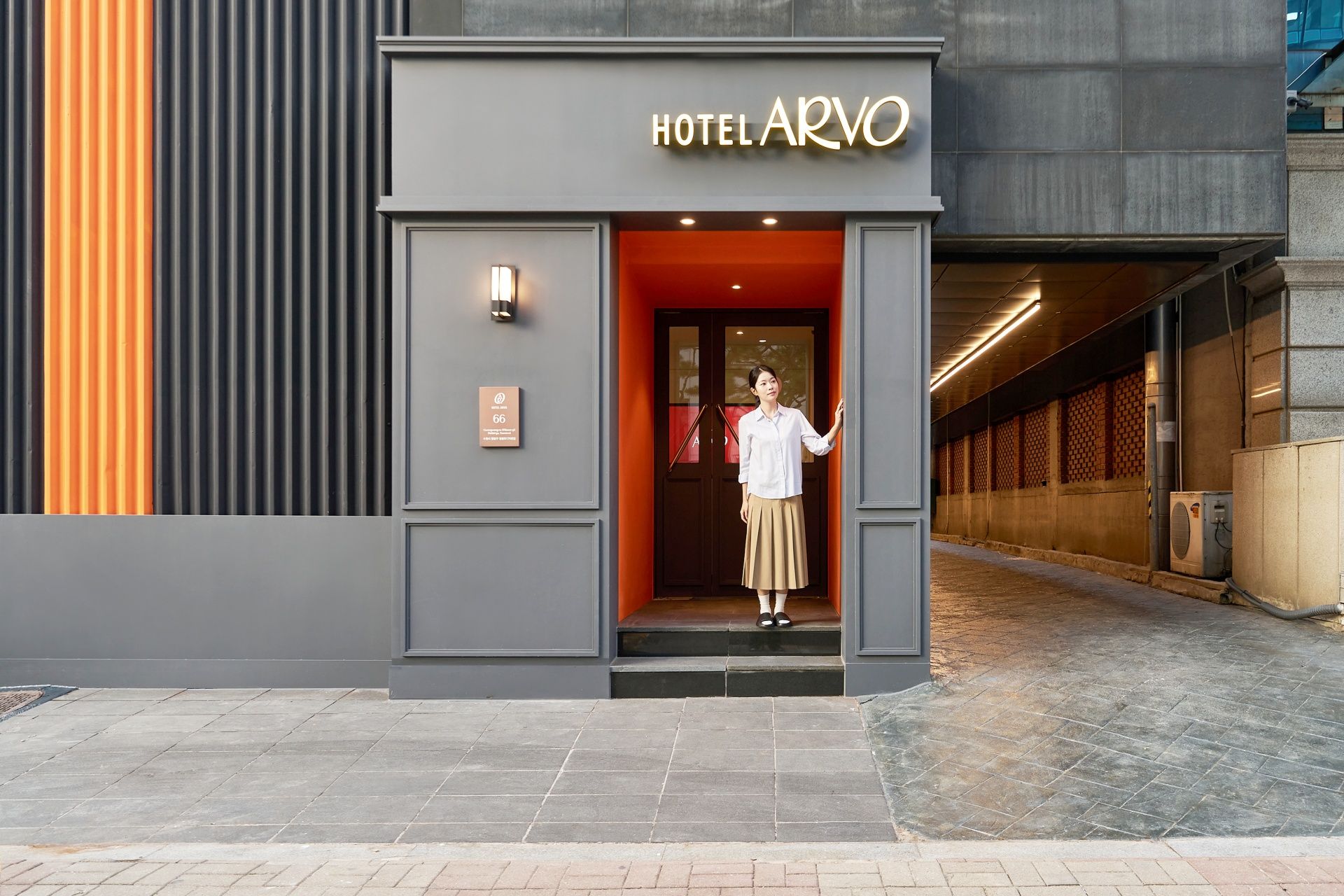 Entrada de un hotel con fachada moderna, un letrero que dice 'HOTEL ARVO' y un cartel con el número de habitación 66.