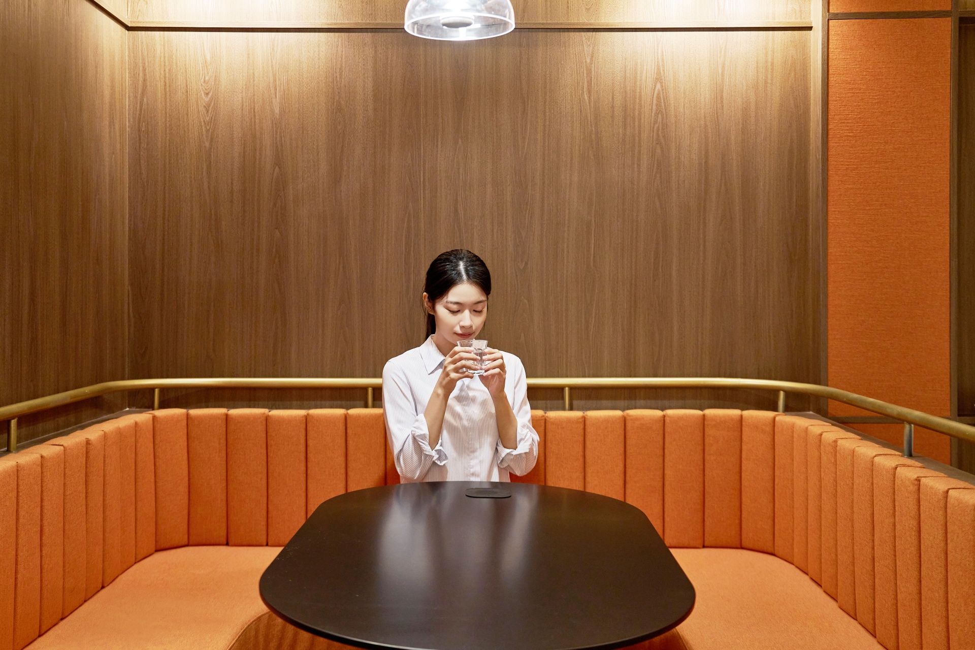 A person seated at a table in a room with wooden paneling and orange cushioned seating.