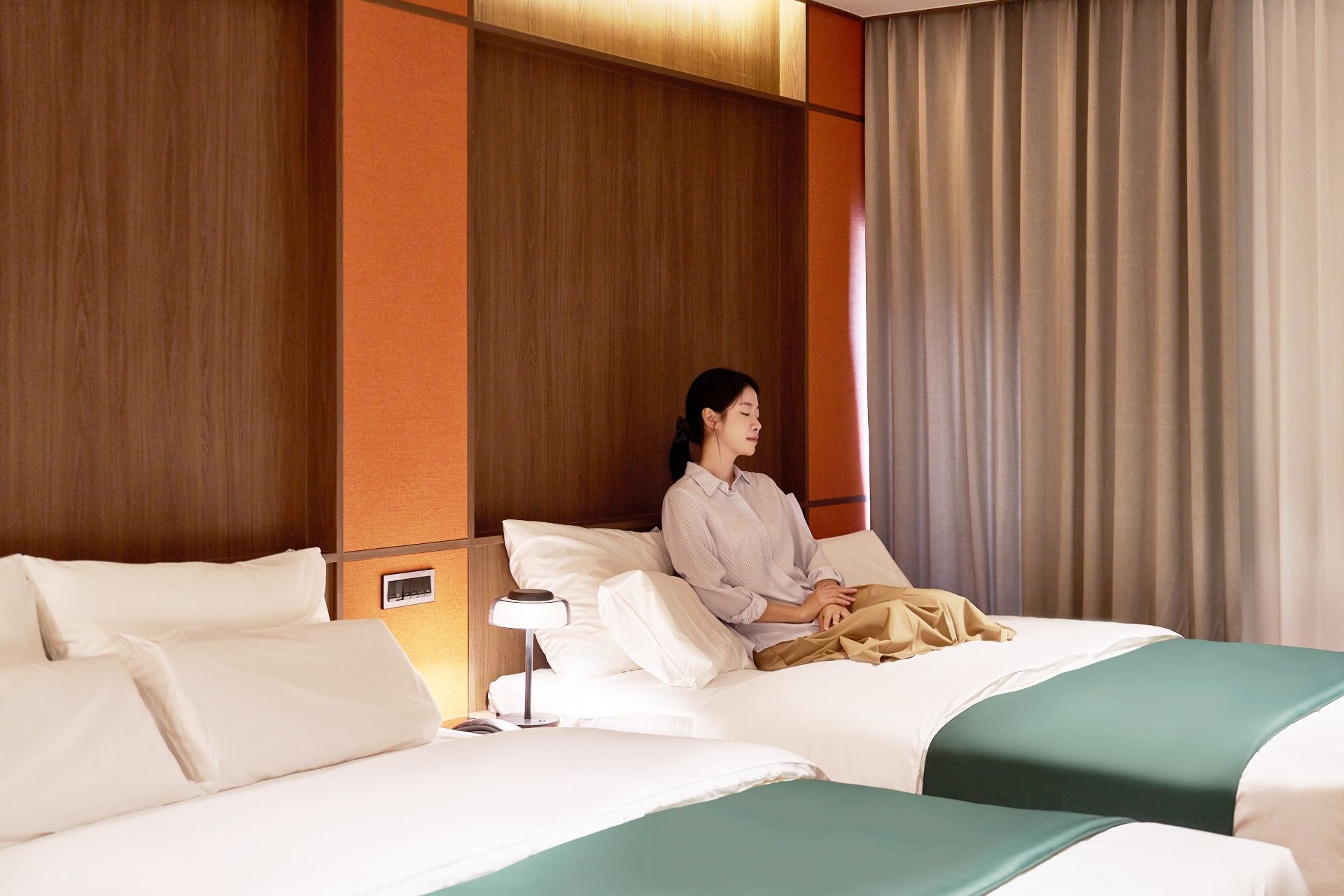 Quarto de hotel com duas camas, mesa de cabeceira e abajur.
