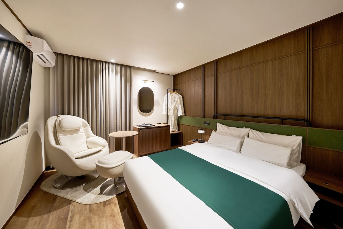 Habitación de hotel con cama, zona de estar con una silla, una mesita, bata y espejo.