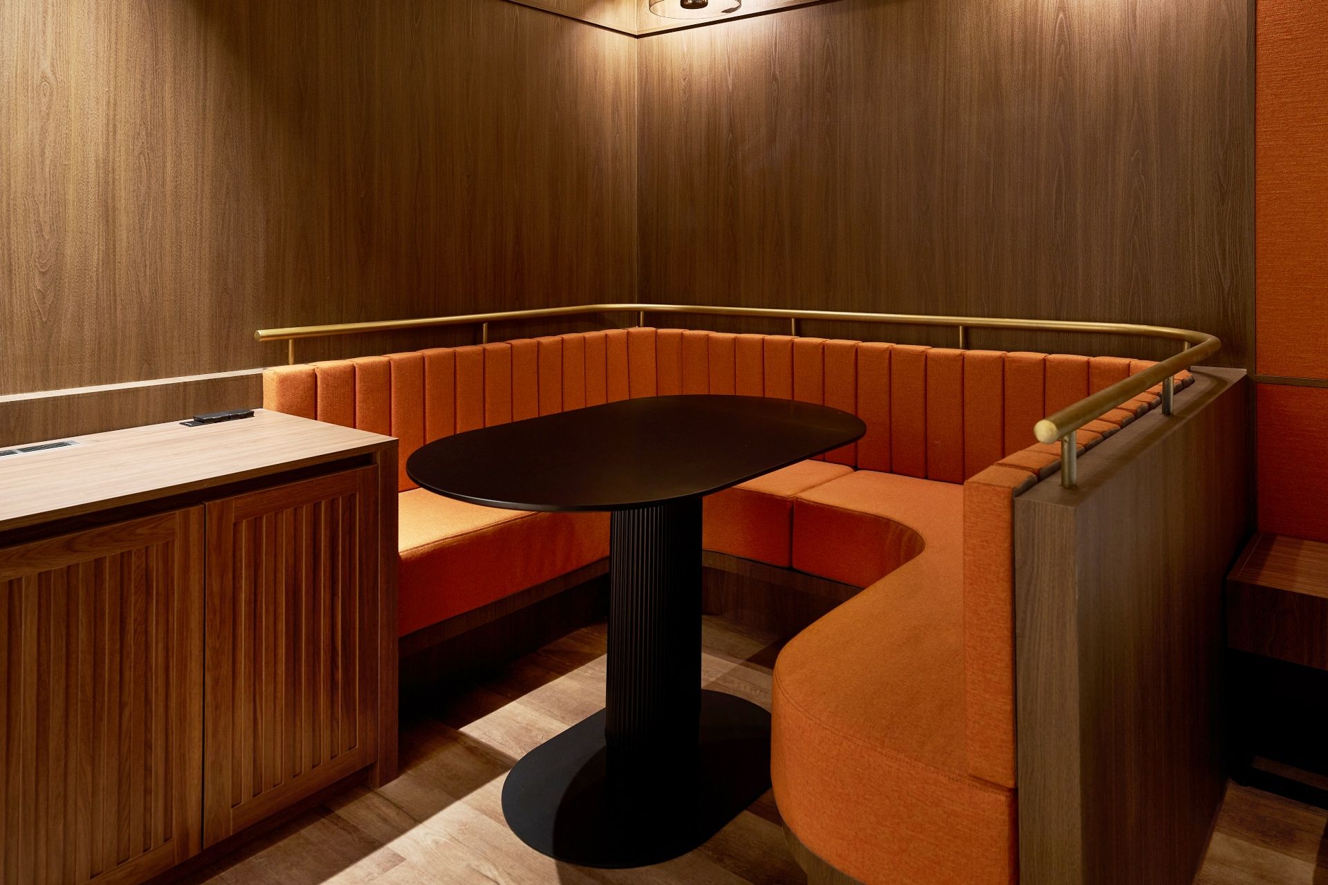 A corner seating area with a wooden panel wall, a small round table, and a cushioned bench.