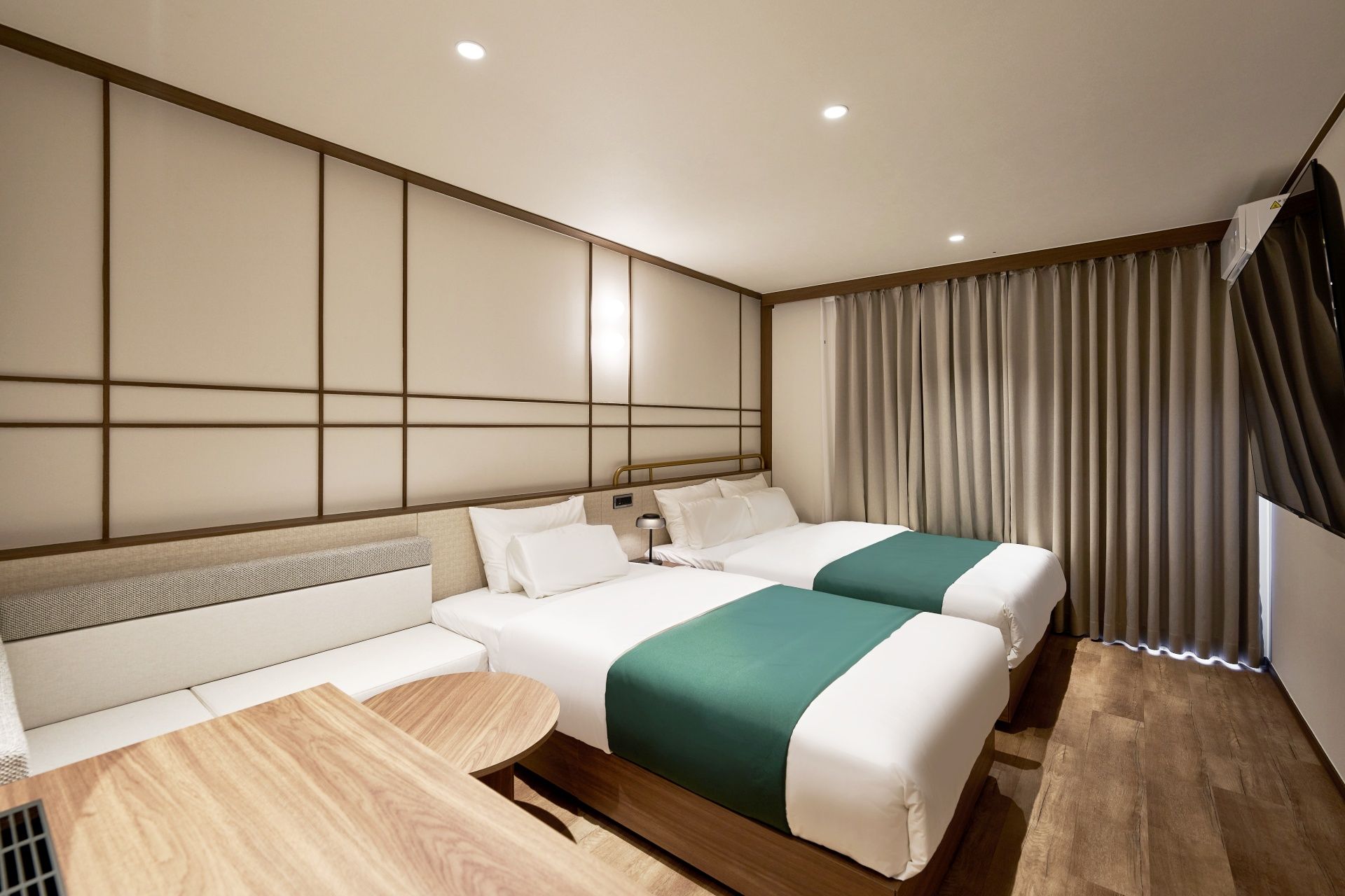 A hotel room with two beds, a sofa, a small table, and a view of the outside.