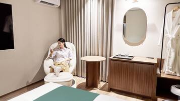 A hotel room with a bed, a round table, a wooden cabinet, a mirror, and a hanging robe.
