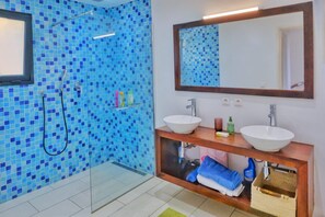 A bathroom with a glass shower enclosure, two sinks, a mirror, and a towel rack. - Villa Marines (nosy be)