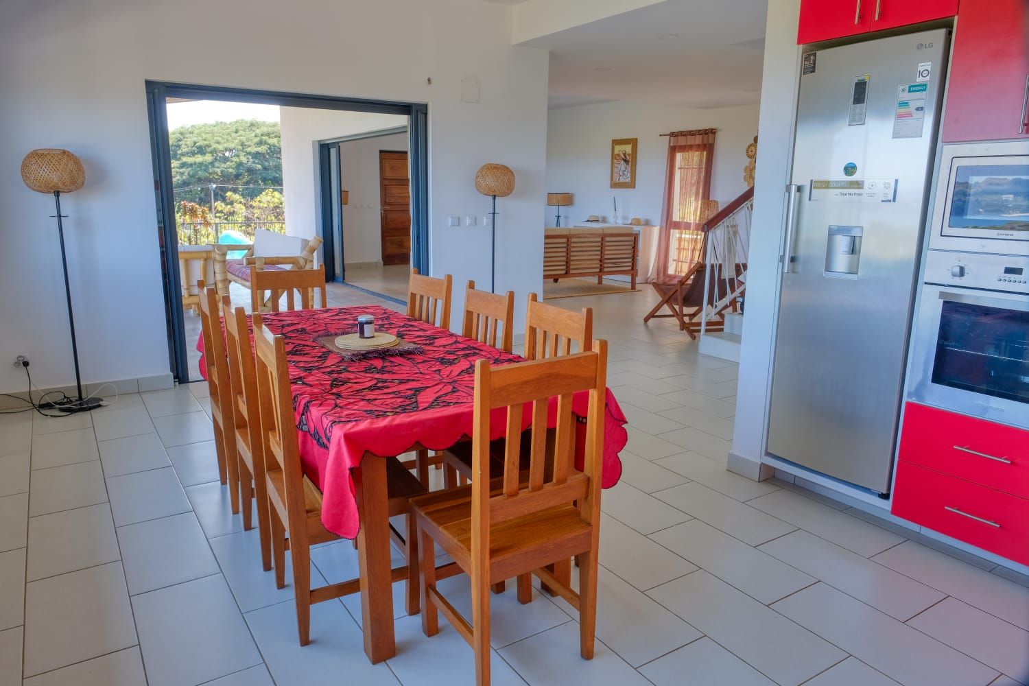 A dining area with a table set for four, wooden chairs, a red tablecloth, and a modern kitchen with red cabinets and a stainless steel refrigerator.