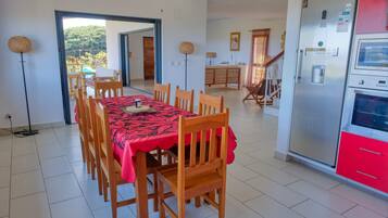 A dining area with a table set for four, wooden chairs, a red tablecloth, and a modern kitchen with red cabinets and a stainless steel refrigerator.