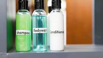 Tres botellas de champú, gel de baño y acondicionador sobre una estantería.