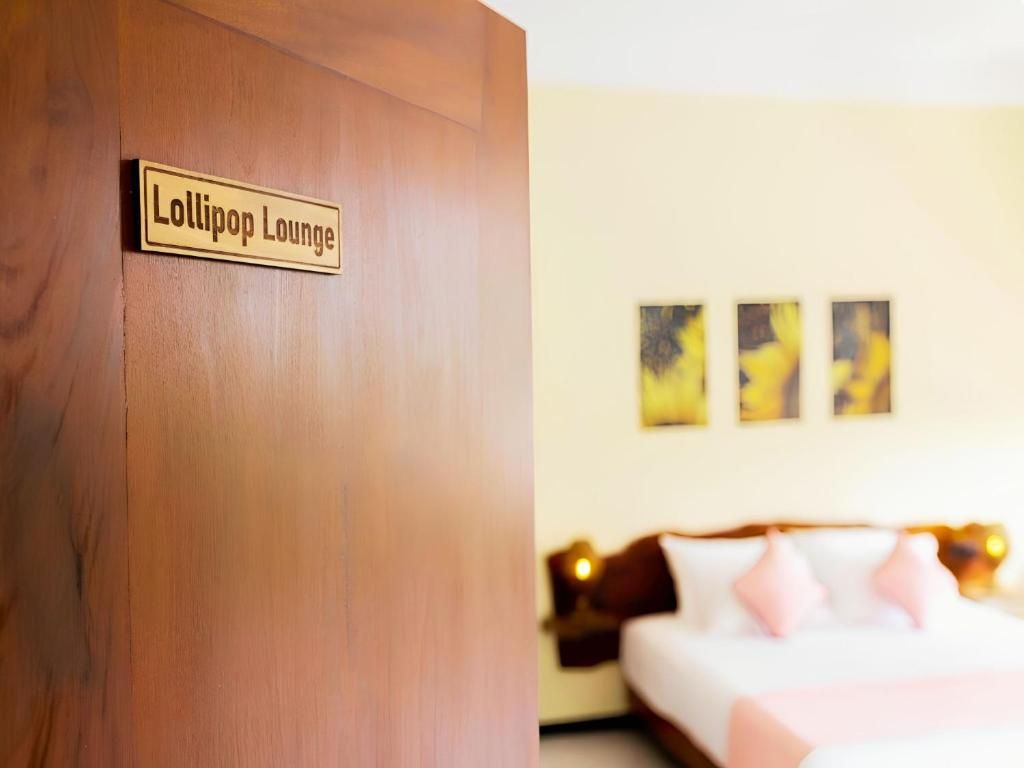 Une chambre d’hôtel avec une porte en bois portant l’inscription « Lollipop Lounge », un lit avec une literie rose et deux tableaux abstraits accrochés au mur.