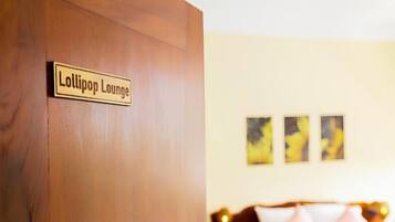 Une chambre d’hôtel avec une porte en bois portant l’inscription « Lollipop Lounge », un lit avec une literie rose et deux tableaux abstraits accrochés au mur.