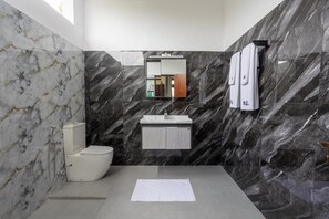 A modern bathroom with a marble wall, a toilet, a sink, and a mirror. - Mashmellow Resort & Spa (Galle)