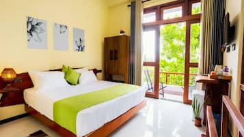 A hotel room with a large bed, a wooden wardrobe, a desk with a chair, and a balcony with a view of greenery.