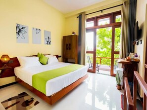 Habitación de hotel con una cama grande, un armario de madera, un escritorio con silla y un balcón con vistas a zonas verdes.