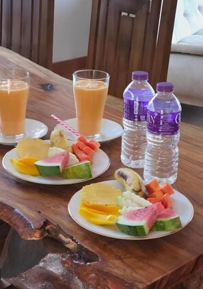 Una mesa de madera con platos de fruta y dos vasos de jugo de naranja, además de dos botellas de agua.