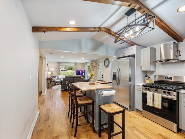 A modern kitchen with a central island, stainless steel appliances, and a wooden ceiling.
