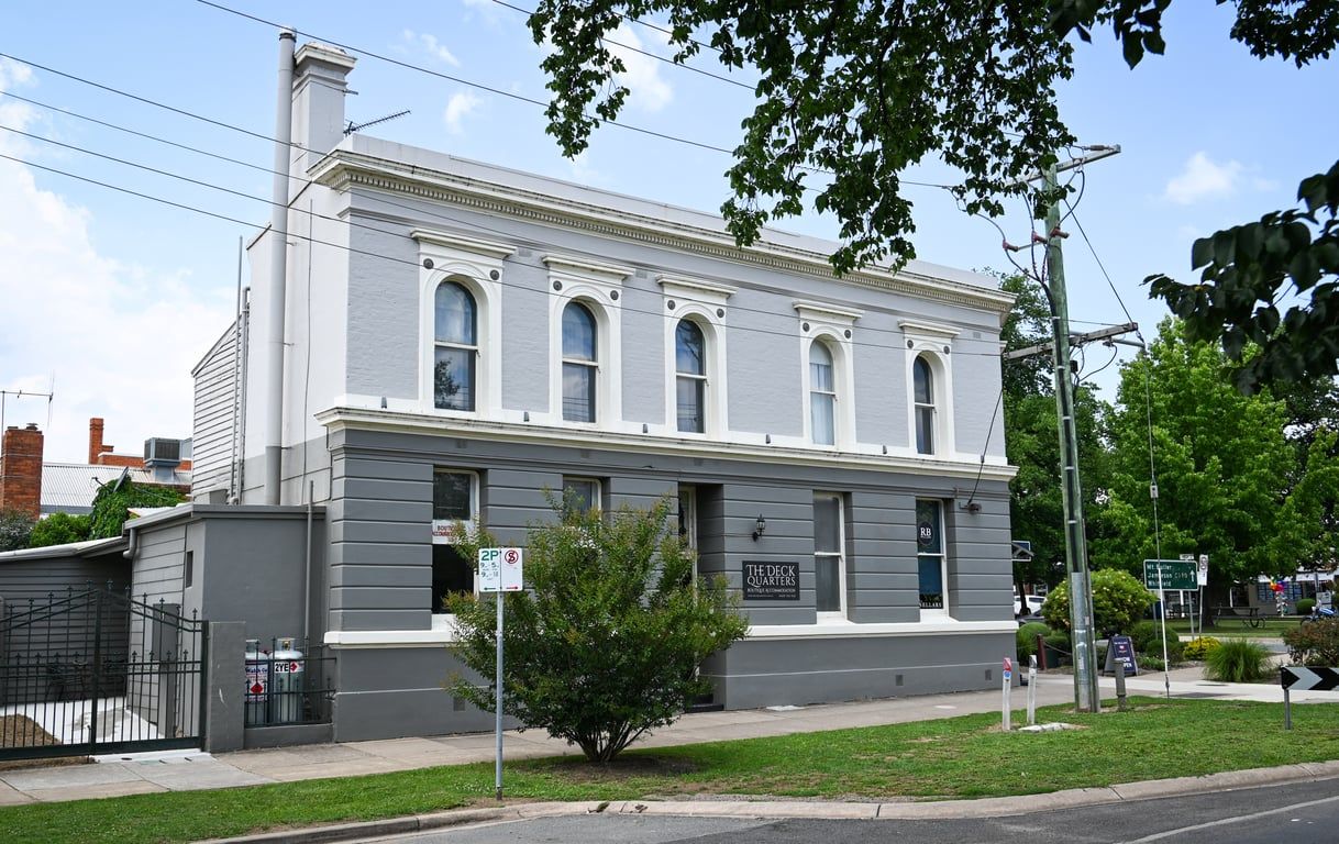 A two-story building with a flat facade, a small front porch, and a sign indicating 'The Deck Quarters.'