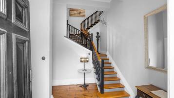 A staircase with wooden steps and black railings, a small round table with a lamp, and a mirror on the wall.