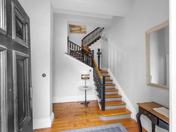 A staircase with wooden steps and black railings, a small round table with a lamp, and a mirror on the wall.