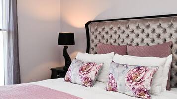 A bedroom with a tufted headboard, a bedside table with a lamp, and floral-patterned pillows.
