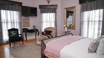A bedroom with a large bed, a chair, a television, and a mirror.