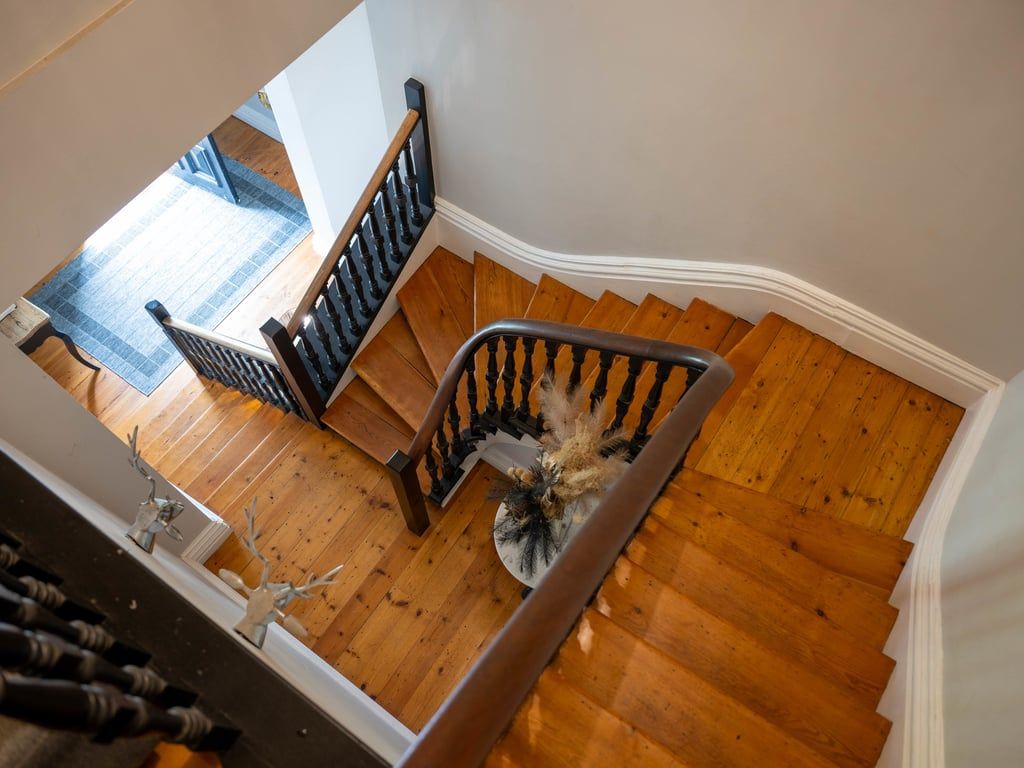 A wooden staircase with a handrail, leading to a landing with a blue carpet.