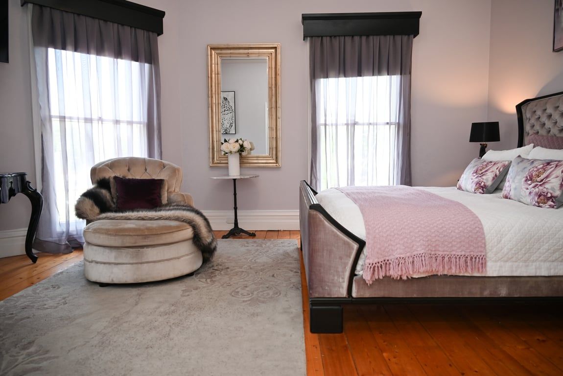 A bedroom with a bed, a chair, a mirror, and a nightstand.