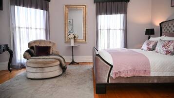 A bedroom with a bed, a chair, a mirror, and a nightstand.