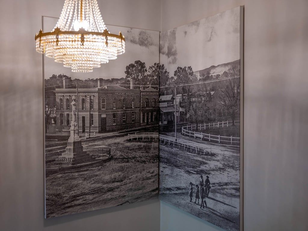 A room with a large framed historical photograph on the wall, a chandelier, and a view of a building.