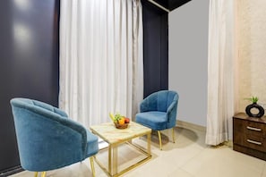 A room with two blue armchairs, a small table with a fruit basket, and a cabinet with a plant. - Hotel Priyaj  (Jaipur)