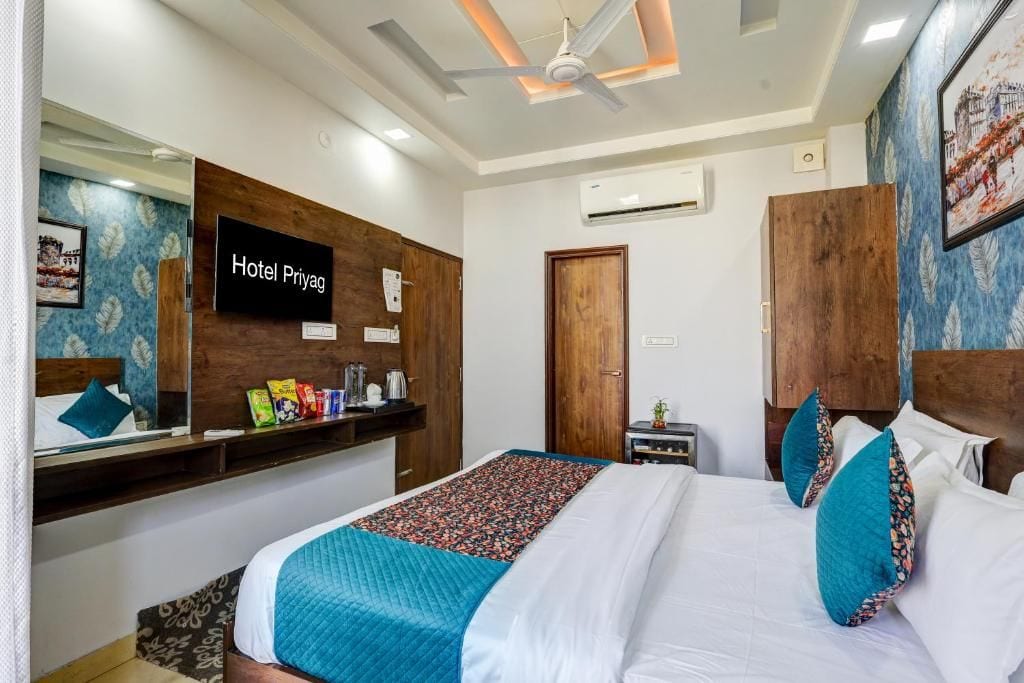 Quarto de hotel com cama, escrivaninha, espelho e televisão na parede.