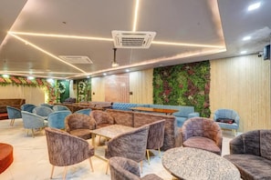 A modern lounge area with plush seating, a long table, and a decorative wall with greenery. - Hotel Priyaj  (Jaipur)