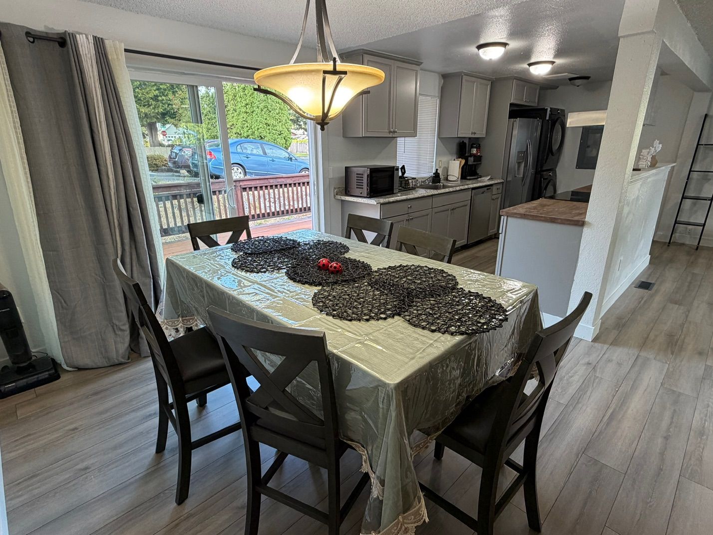 Un coin repas avec une table dressée pour quatre personnes, une cuisine en arrière-plan et une vue sur l’extérieur.