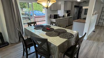 A dining area with a table set for four, a kitchen in the background, and a view of the outside.