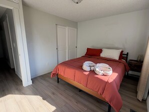 Un dormitorio con cama, almohadas, una mesita de noche y una puerta.