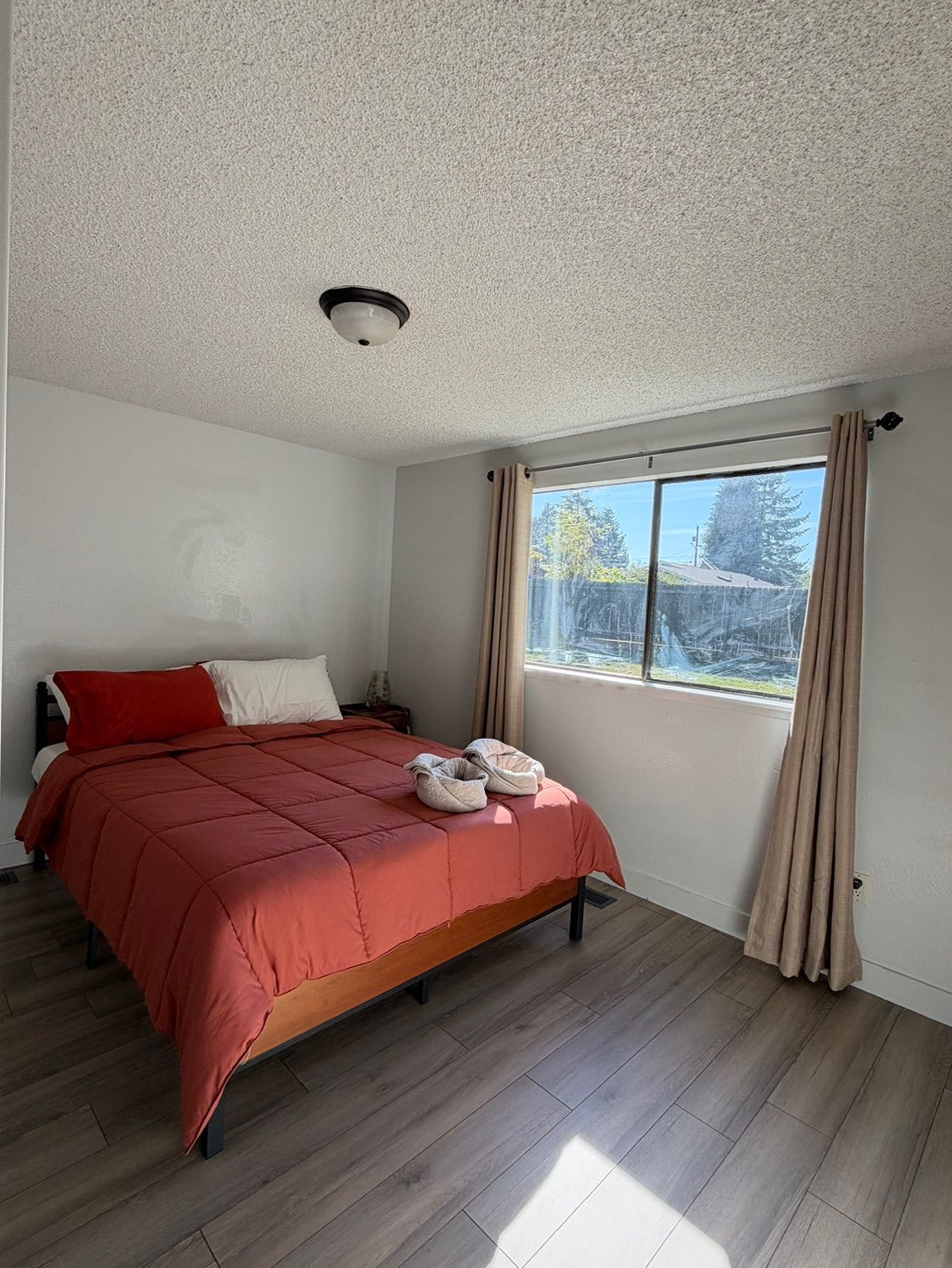 A bedroom with a bed, a window with curtains, and a ceiling light.